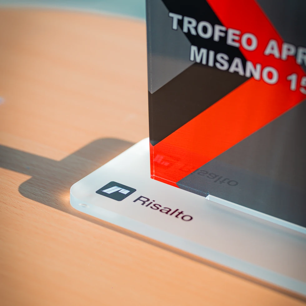 Dettaglio della base satinata di un trofeo personalizzato riportante il logo "Risalto" su un tavolo in noce